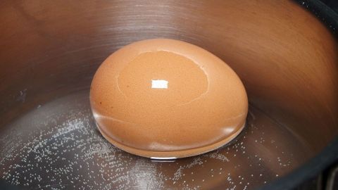 Ein Ei liegt in einem Topf, während es gekocht wird. Der Topf hat eine glänzende, metallische Oberfläche und ist leer.