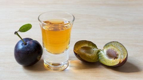 Ein Glas Pflaumenlikör steht auf einem Holztisch neben einer frischen und einer halbierten Pflaume.