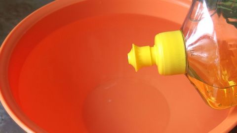 Mit diesem Tipp werden Fenster und Spiegel schmierfrei sauber. Ein Flasche mit Gel reinigt wird über eine orangefarbene Schüssel gehalten, bereit zum Mischen für schmierefreie Fenster.