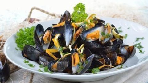 Miesmuscheln liegen in einer Schüssel, garniert mit Kräutern und Zitronenscheiben auf einem Tisch mit Stoffserviette.