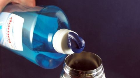 Eine Hand gießt blauen Spülmaschinen-Klarspüler in die Öffnung einer Thermoskanne zur Reinigung.