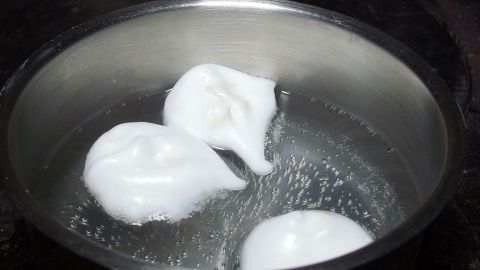 Drei schaumige Eiweißkugeln schwimmen in einem Topf mit kochendem Wasser, bereit zum Garen für das Dessert.