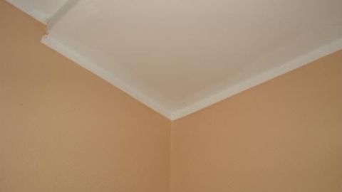 Ein sauberer Wandrand wird gezeigt, wo die weiße Decke auf die beige Wand trifft, ohne Farbkleckse.