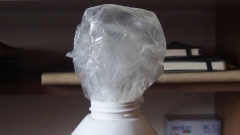 Eine Plastikflasche hat eine Folienverpackung als Deckel, um den Volumen von Folienmüll zu reduzieren. Im Hintergrund sind einige Bücher zu sehen.