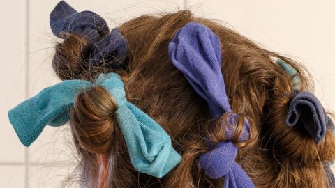 Socken werden als Haarklammern verwendet, um die Locken zu formen. Die Umgebung ist hell und neutral.
