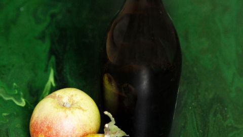 Eine Flasche Apfelessig steht neben zwei Äpfeln auf einem grünen, marmorierten Hintergrund.
