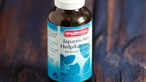 Eine dunkelbraune Flasche mit Minzöl steht auf einem Holzuntergrund. Das Etikett beschreibt die Anwendung bei Kopfschmerzen.