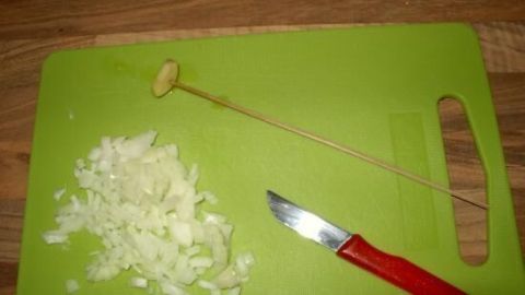 Eine grüne Schneidefläche zeigt gehackten Knoblauch und ein Schneidewerkzeug, bereit für das Kochen in der Pfanne.