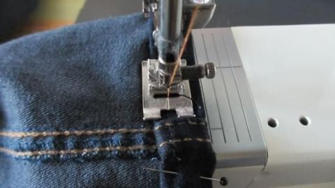 Eine Nähmaschine näht dicke Stoffe, während der Nähfuß über den Stoff gleitet und präzise Stiche setzt.