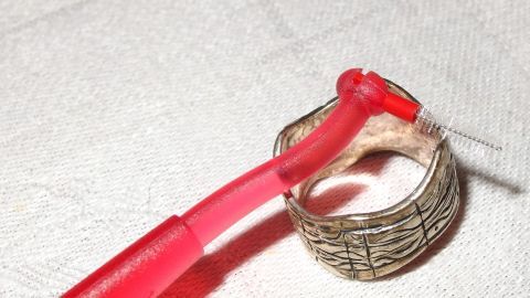 Ein Interdentalbürste reinigt Silberschmuck, während sie auf einem hellen Tuch liegt, um Schmutz zu entfernen.