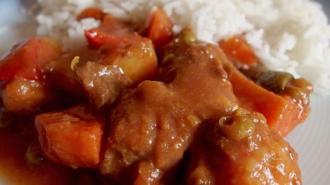 Ein herzhaftes Kürbis-Paprika-Gulasch liegt auf einem Teller neben einer Portion Reis und vermittelt ein warmes, appetitliches Gefühl.