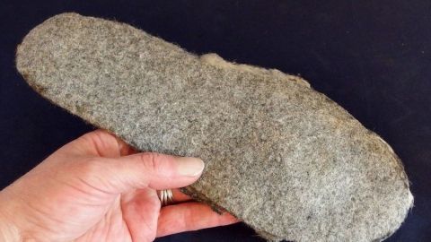Eine Hand hält eine warme Einlegesohle aus Wollfilz, umgeben von einem dunklen Hintergrund.