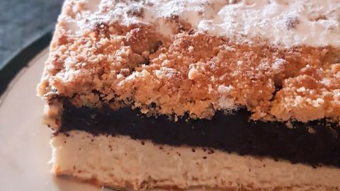 Ein Stück Apfel-Quark-Mohnkuchen mit Streuseln liegt auf einem Teller, daneben eine Gabel. Die Umgebung ist hell und gemütlich.