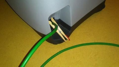 Ein grünes Staubsaugerkabel ist an einer Wand im Staubsauger befestigt und rollt sich ungewollt ein, während der Untergrund gelb ist.