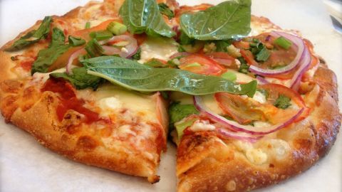 Eine leckere Pizza ist in Stücke geschnitten und wird mit frischen Zutaten wie Salat garniert, serviert auf einem weißen Teller.