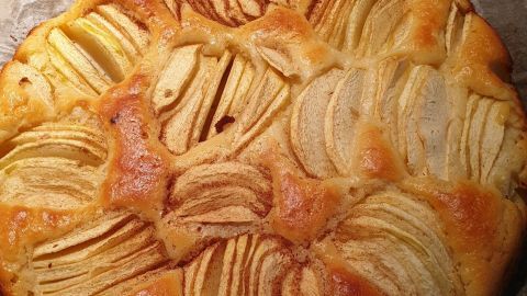 Ein frisch gebackener Apfel-Quark-Kuchen mit glänzenden Apfelscheiben liegt auf Backpapier und ist bereit zum Servieren.