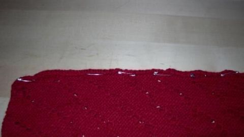Rote Strickteile liegen auf einem Tisch und werden mit Stecknadeln festgesteckt, bereit zum Zusammennähen in einem kreativen Prozess.