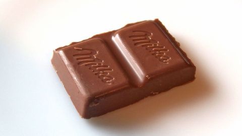 Gegen Halsschmerzen ein Stück Schokolade langsam im Mund zergehen lassen. Eine Schokoladentafel liegt auf einem weißen Teller, warm und einladend, ideal bei Halsschmerzen zur Linderung.