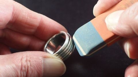 Eine Hand hält einen Ring, während die andere mit einem Radiergummi über ihn reinigt. Der Hintergrund ist dunkel.
