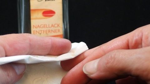 Eine Hand hält ein Wattepad, das mit Nagellackentferner benetzt ist, während es über die Haut reibt, um Nikotinflecken zu entfernen.