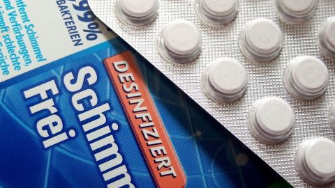 Weiße Tabletten und ein Desinfektionsmittel sind nebeneinander auf einer Oberfläche platziert, was kindersicheres Verwahren verdeutlicht.