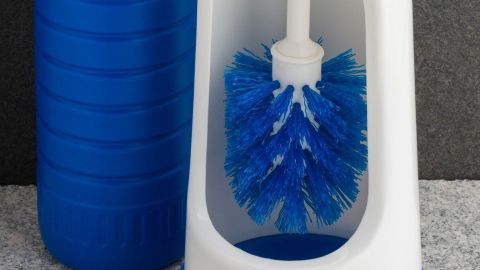 Eine Klobürste steht in einem blauen Halter, bereit zum Reinigen, neben einer blauen Flasche in einem Badezimmerumfeld.