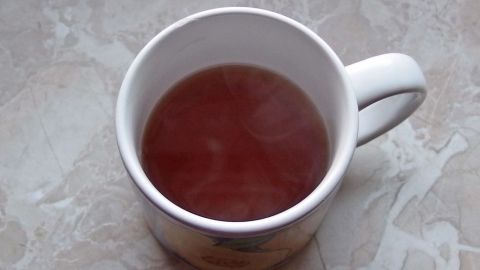 Eine Tasse Tee steht auf einem Tisch, dampfend und heiß, umgeben von einem schlichten, hellen Untergrund.