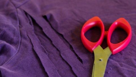 Ein lila T-Shirt liegt auf einem Holztisch, während eine Schere daneben liegt, bereit für das Schneiden.