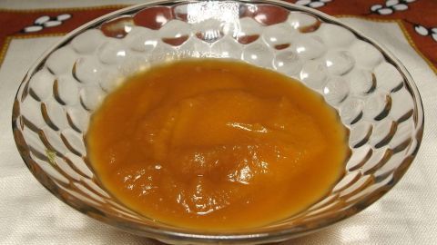 Apfelmus oder Apfelkompott mit Ingwer und Zitronensaft. Das Ergebnis: fruchtig-leicht scharf, sehr lecker! Ein Glas mit Apfelmus steht auf einem Tisch mit hellem Tischdecke, umgeben von einem dekorativen Rand im Hintergrund.