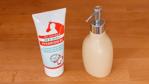 Eine Tube Pferdebalsam steht neben einem Dosierspender, bereit zum Umfüllen auf einer Holzoberfläche.