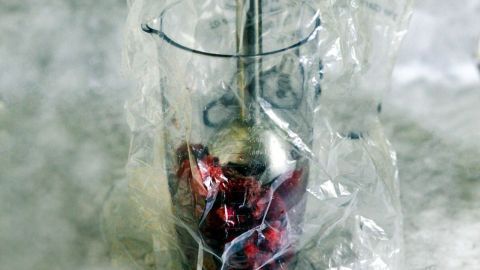 Ein Pürierstab steht in einem transparenten Becher, der mit einer Plastikfolie umwickelt ist, um Spritzer zu vermeiden.