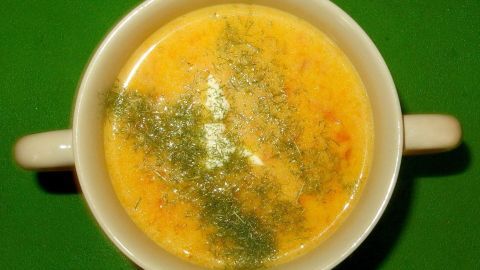 Eine Schüssel feine Butternusskürbis-Suppe steht auf einem grünen Tisch, glänzend mit frischen Kräutern garniert.