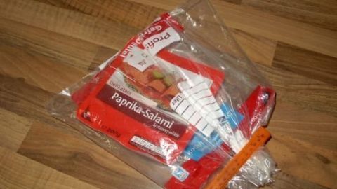 Eine Packung Paprikasalami liegt in einer durchsichtigen Tüte auf einer Holzoberfläche zur hygienischen Aufbewahrung.