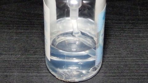 Eine transparente Flasche enthält flüssige Handseife und steht auf einer dunklen Oberfläche in einem neutralen Umfeld.