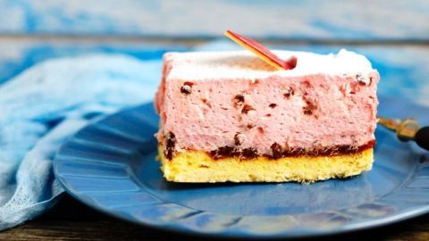 Ein Stück Torte mit einer bunten Gelatinefüllung liegt auf einem blauen Teller, umgeben von einer rustikalen Holzoberfläche.