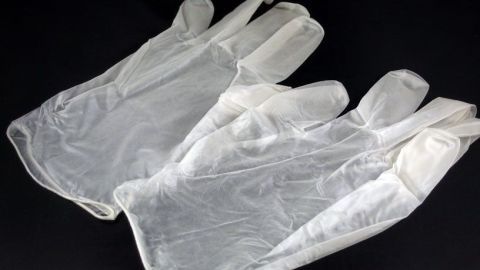 Latex Einweghandschuhe liegen zusammengeklebt auf einem dunklen Untergrund, bereit für den Einsatz.