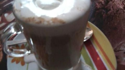 Eine Tasse kalten Kaffee steht auf einem bunten Unterteller, während dampfender Schaum sichtbar wird.