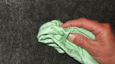 Eine Hand hält ein grünes Reinigungstuch, das einen Milchfleck von einer dunklen Oberfläche entfernt.