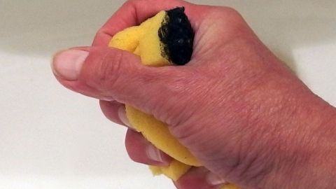 Eine Hand drückt einen gelben Wischschwamm aus, der über einem Waschbecken gehalten wird.