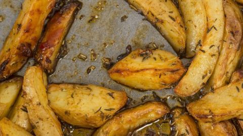 Goldbraune Blechkartoffeln liegen auf einem Blech und sind knusprig gebacken, umgeben von aromatischen Kräutern.