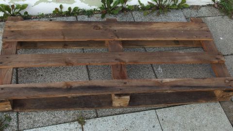 Ein stabiler Holzpalette liegt auf einem Pflastersteingelände, bereit zur Nutzung zum Schutz großer Elektrogeräte vor Wasserschäden.