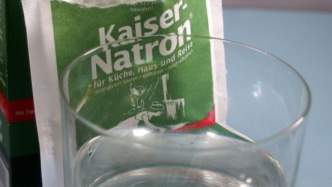 Ein Glas Wasser steht vor einer offenen Tüte mit Kaiser-Natron, bereit für die Anwendung bei empfindlichen Zahnhälsen.