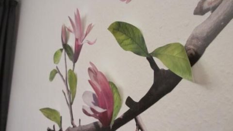 Auf einer Wand sind plastisch wirkende Blüten und Blätter angebracht, die lebendig und dreidimensional erscheinen.