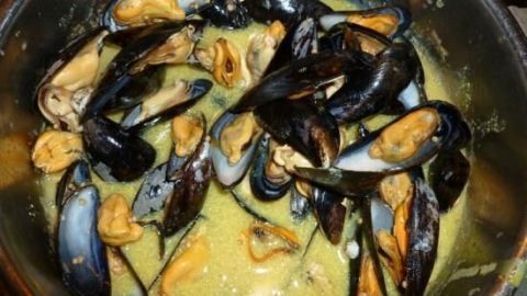 Muscheln liegen in einer cremigen Sauce in einem Topf und zeigen die Zubereitung des Mouclade-Gerichts.
