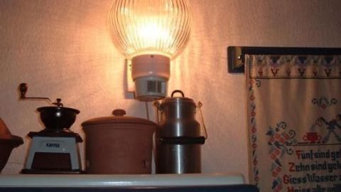 Eine Lampe mit Bewegungsmelder leuchtet über Küchenschränken, umgeben von Küchenutensilien und einem gemusterten Vorhang.