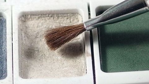 Ein Pinsel hebt einen glänzenden Lidschatten in einer Palette an, um ihn gleich aufzutragen, um längerhaltende Farbe zu zeigen.