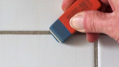 Ein Radiergummi wird verwendet, um die hellen Fliesenfugen zu reinigen, während eine Hand das Werkzeug sicher führt.