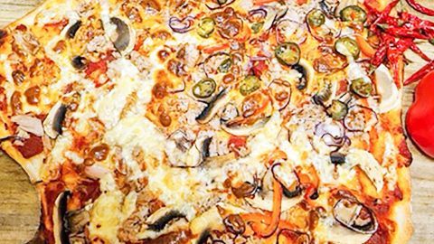 Eine große Seemannspizza liegt auf einem Holzbrett und ist reich garniert mit verschiedenen Zutaten und Gewürzen.