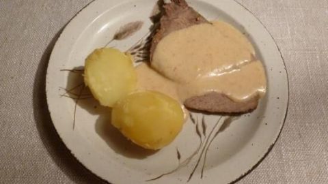 Zarte Rinderhüfte wird mit einer cremigen Meerrettichsauce und zwei gekochten Kartoffeln auf einem Teller serviert.