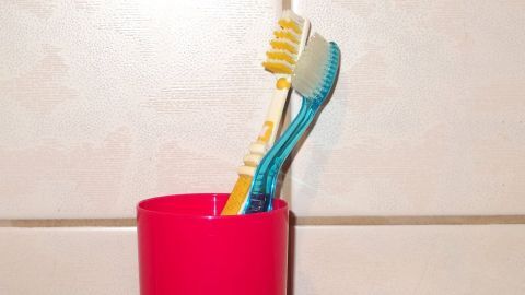 Ein Zahnputzbecher steht auf einer Fliese, zwei Zahnbürsten ragen heraus, bereit zum Zähneputzen und Wasser sparen.